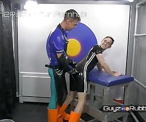 Two guys in tight shiny rubber  orange boots arse fingering jerking each other dildos rimming